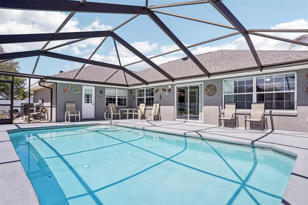 A swimming pool with a screened enclosure sits on a patio behind a gray house — 5353 COUNTY ROAD 125, WILDWOOD, FL