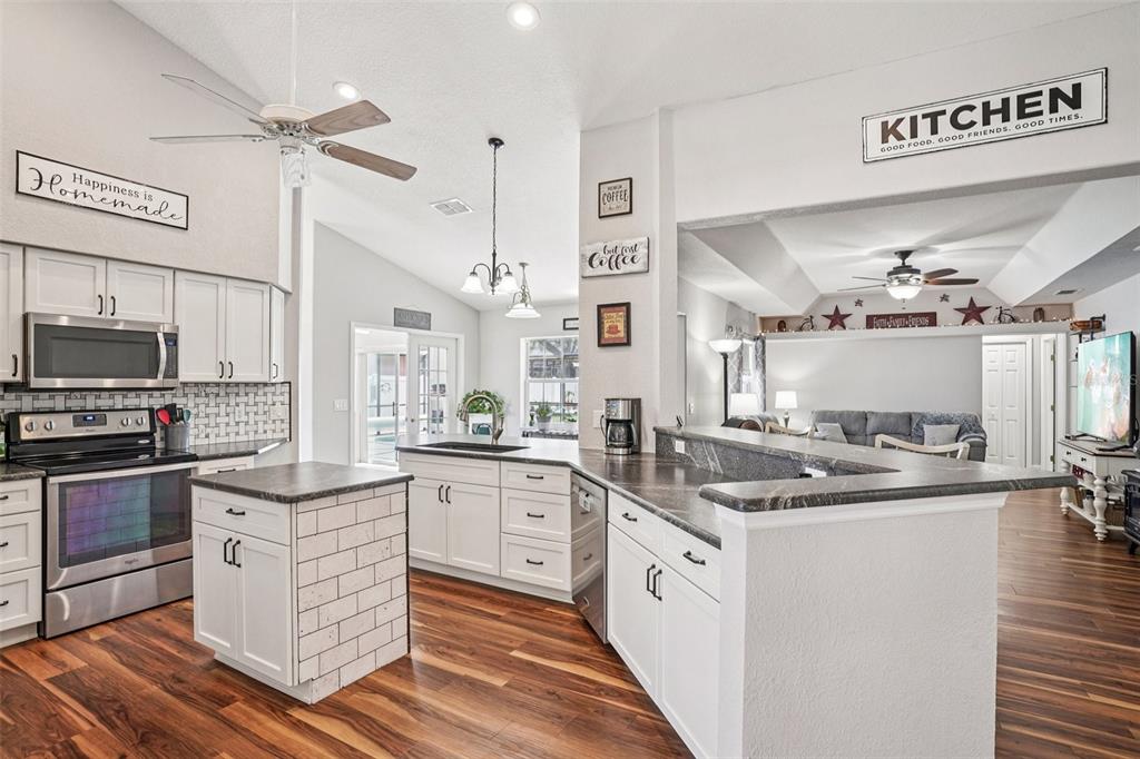 A kitchen with white cabinets, dark countertops, and a center island overlooks a living area — 5353 COUNTY ROAD 125, WILDWOOD, FL