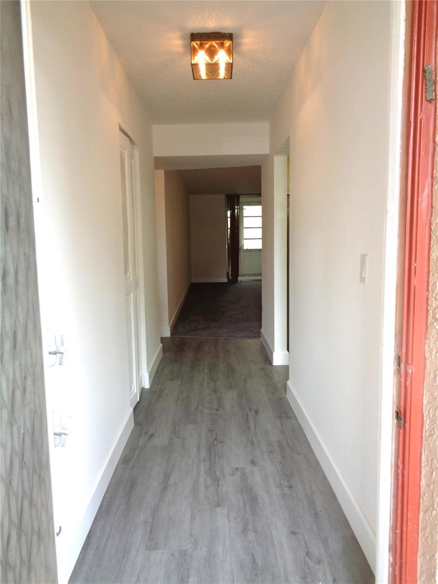 A hallway with gray wood-look flooring leads to a carpeted room with a glass door — 7320 Lake Circle Drive # 101, Margate FL 33063, MARGATE, FL