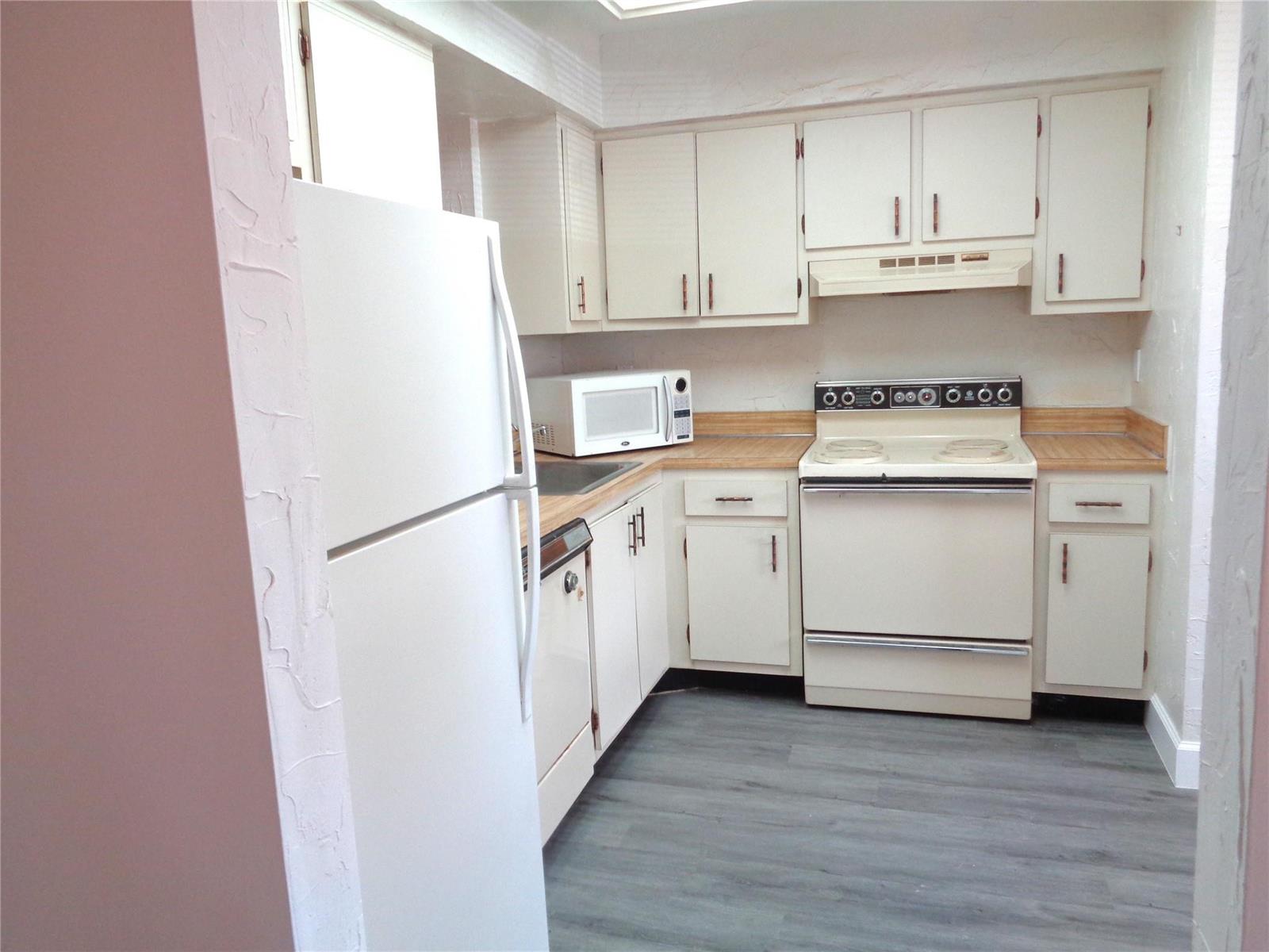 A kitchen features white cabinets, a white refrigerator, a stove, and grey wood-look flooring — 7320 Lake Circle Drive # 101, Margate FL 33063, MARGATE, FL