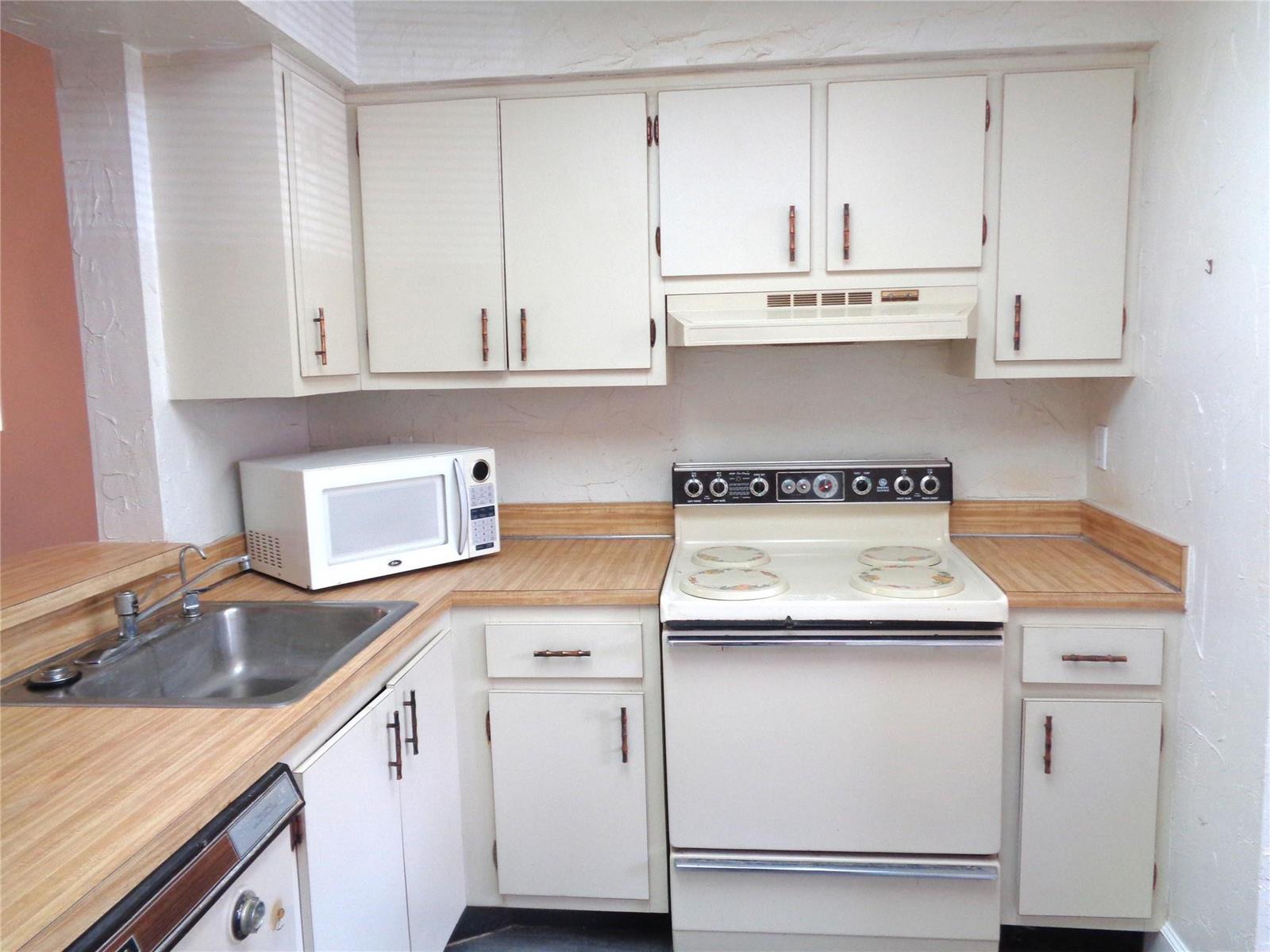 A kitchen features white cabinets, a stainless steel sink, a microwave, and a white stove — 7320 Lake Circle Drive # 101, Margate FL 33063, MARGATE, FL