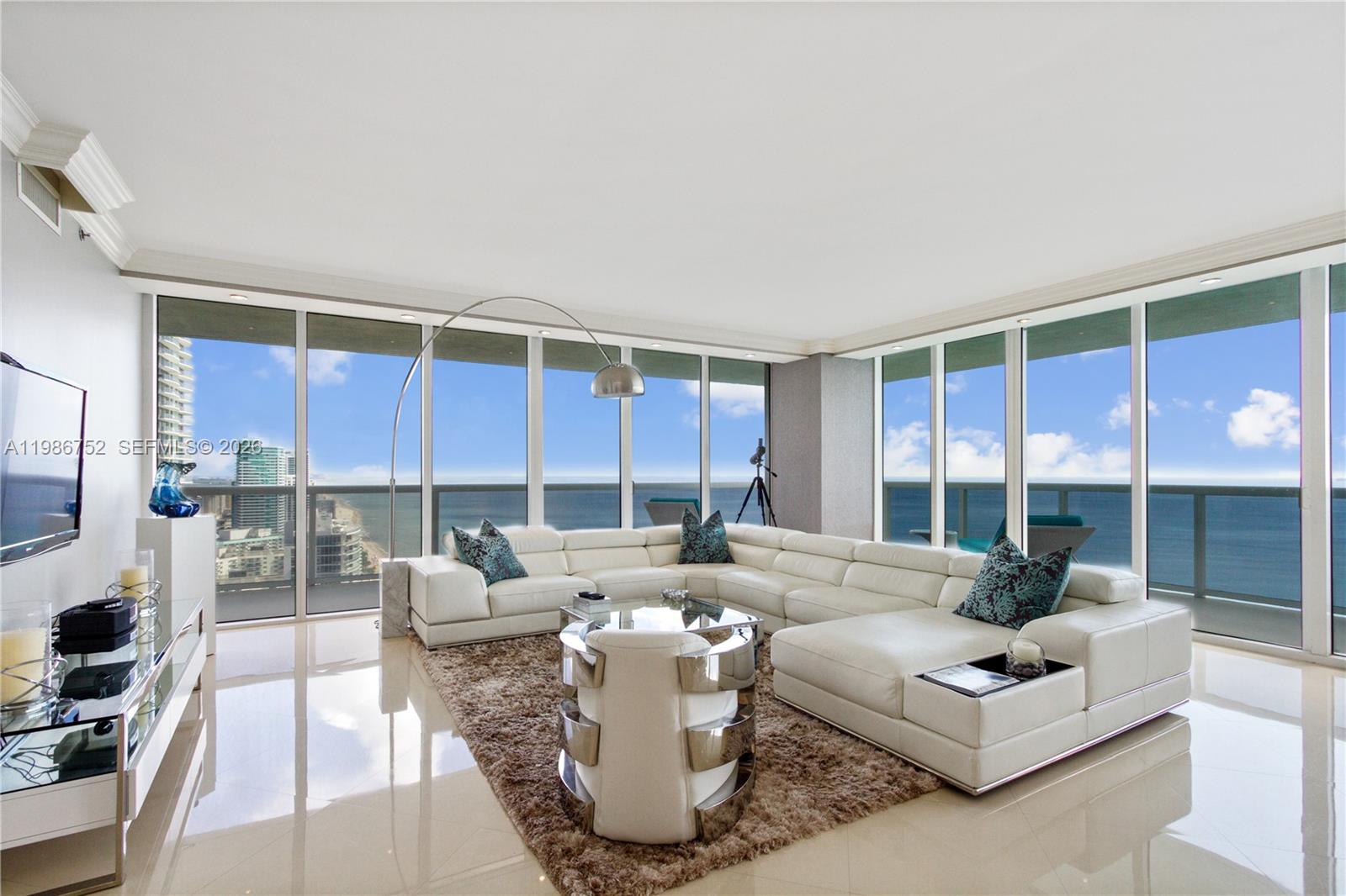 A modern living room features a white sectional sofa, a glass coffee table, and floor-to-ceiling windows — 1830 S Ocean Dr # 3401, Hallandale Beach FL 33009, HALLANDALE BEACH, FL