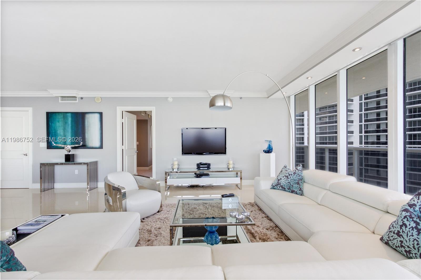 A modern living room features a white sectional sofa, glass coffee table, and floor-to-ceiling windows — 1830 S Ocean Dr # 3401, Hallandale Beach FL 33009, HALLANDALE BEACH, FL