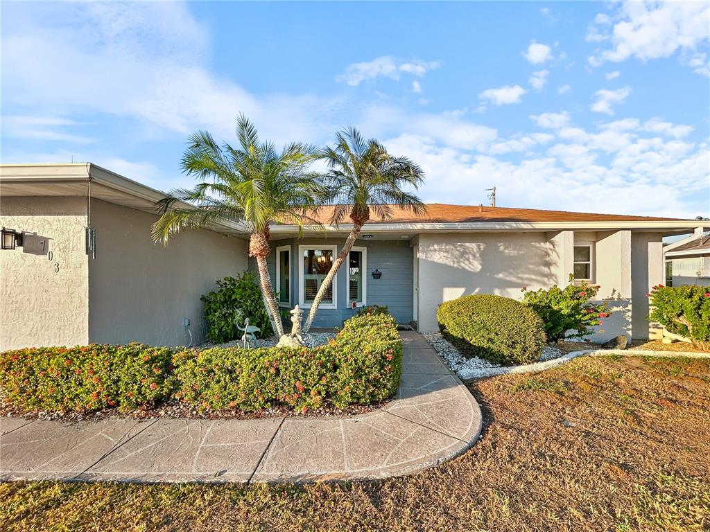 A single-story house with a beige exterior, palm trees, and a curved concrete walkway — 703 OJAI AVENUE, SUN CITY CENTER, FL