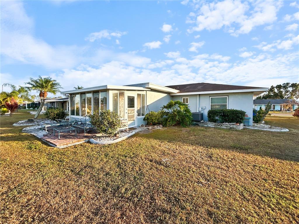 A single-story house with a sunroom, brick patio, and landscaping under a blue sky — 703 OJAI AVENUE, SUN CITY CENTER, FL