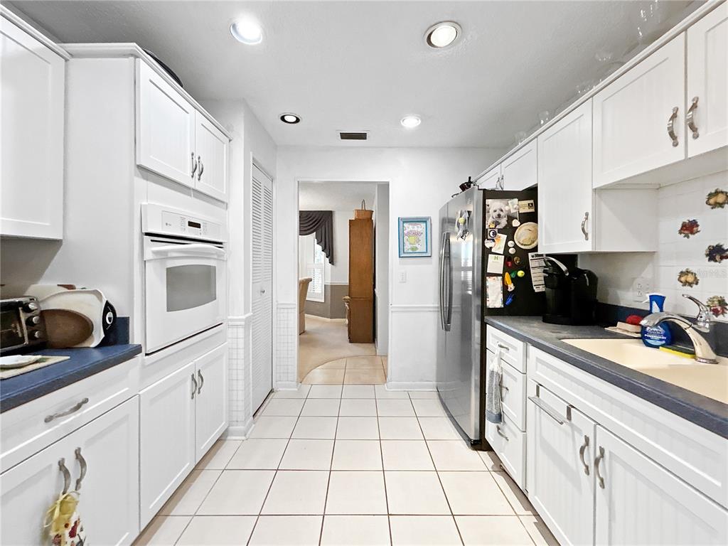 A galley kitchen features white cabinets, stainless steel appliances, and light-colored tiled flooring — 703 OJAI AVENUE, SUN CITY CENTER, FL