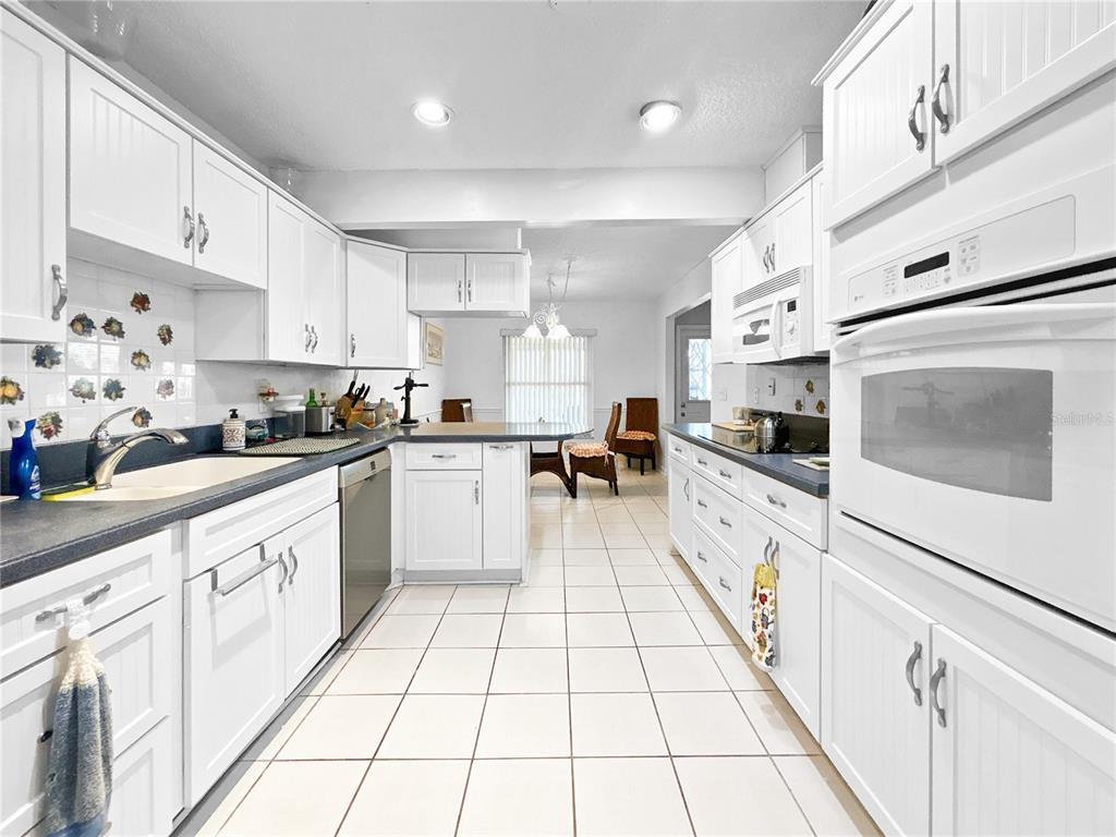 A white kitchen features dark countertops, tile flooring, and a built-in wall oven — 703 OJAI AVENUE, SUN CITY CENTER, FL