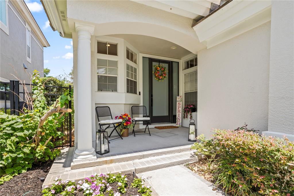 A covered front porch features two metal chairs, a spring sign, and potted flowers — 8455 FOXWORTH CIRCLE UNIT 3, ORLANDO, FL