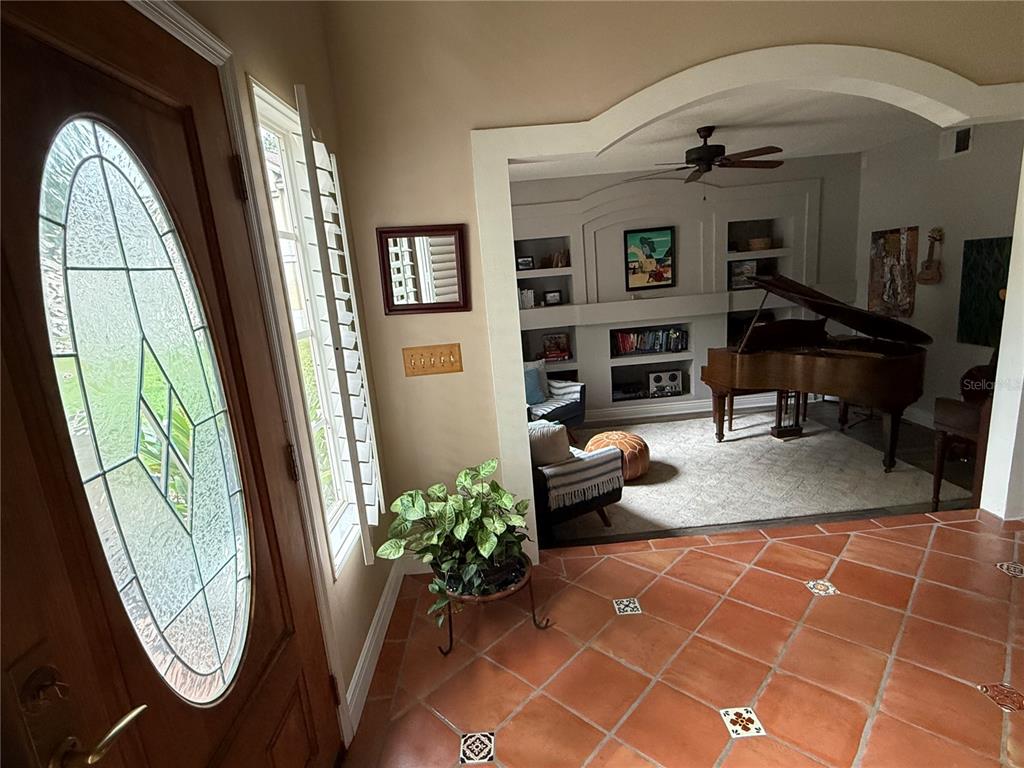 An entryway with terracotta tile floors leads into a living room featuring a grand piano — 1701 BRIDLEWALK COURT, GOTHA, FL