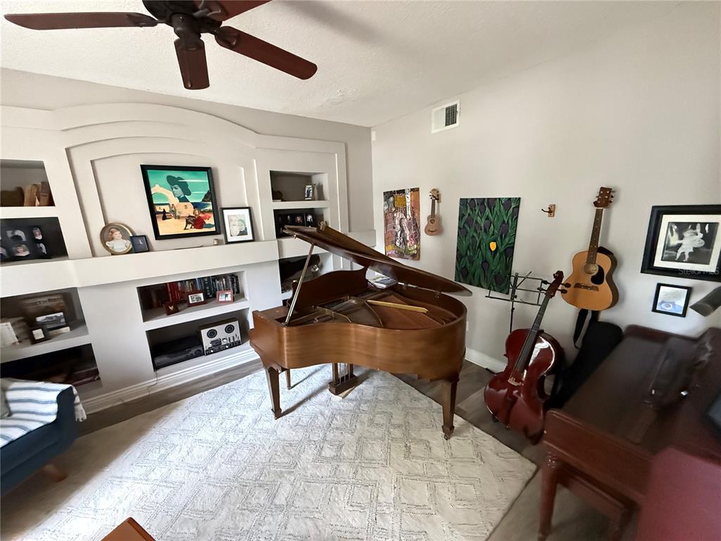 A living room features a grand piano, built-in shelving, and various musical instruments on display — 1701 BRIDLEWALK COURT, GOTHA, FL