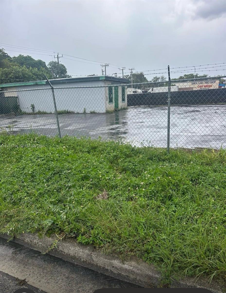 A fenced, paved vacant lot features a small, single-story utility building under a cloudy sky — 11537 NW 27th Ave, Miami FL 33167, MIAMI, FL