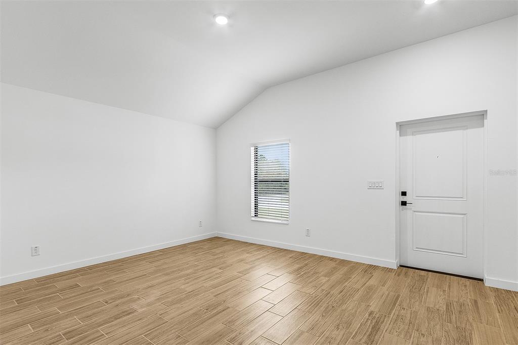 An empty room with white walls, a vaulted ceiling, a window, and wood-look tile flooring — 4562 TAHITI STREET, NORTH PORT, FL