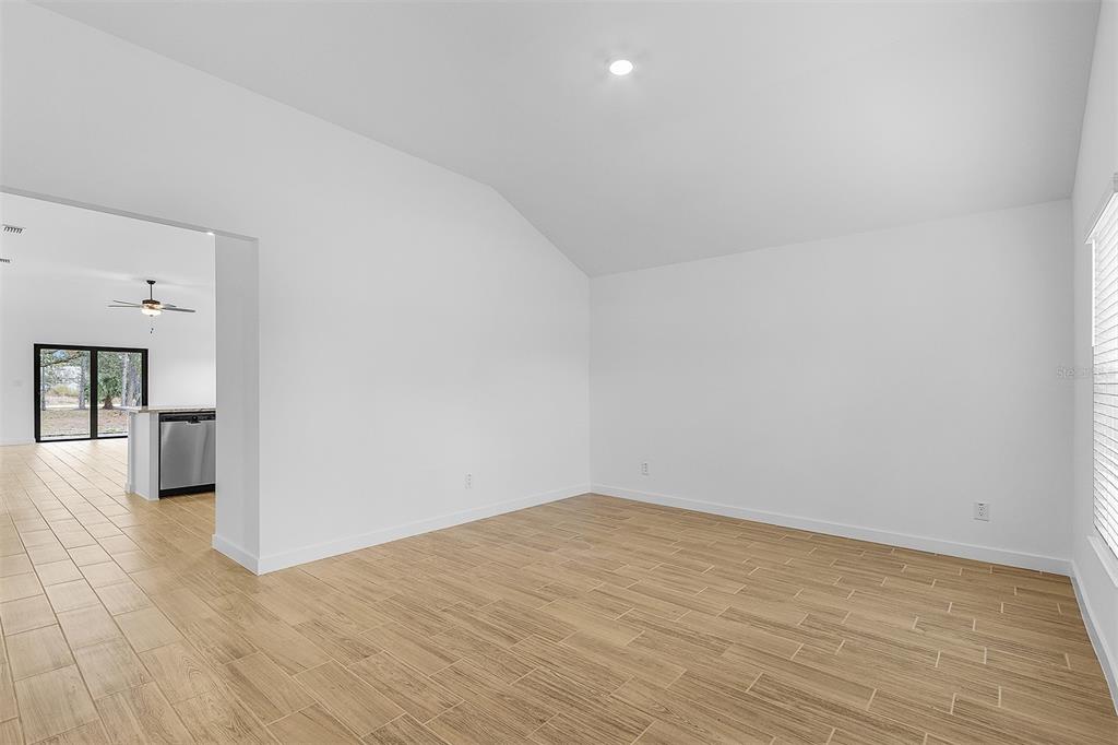 A bright, empty room with vaulted ceilings, white walls, and light-colored wood-look tile flooring — 4562 TAHITI STREET, NORTH PORT, FL