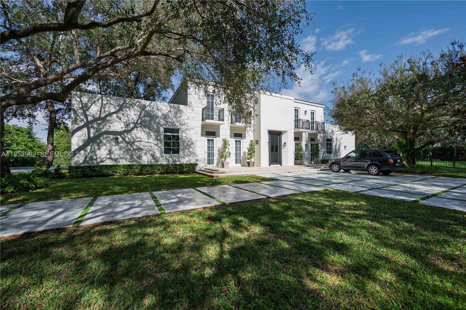 A two-story white stucco house features a modern driveway and black metal balcony railings — 6355 SW 114th St, Pinecrest FL 33156, PINECREST, FL