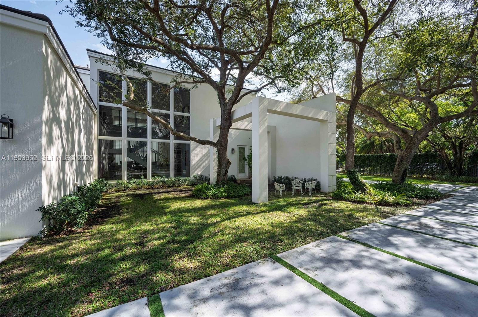 A modern white house exterior features large floor-to-ceiling windows and a covered patio area — 6355 SW 114th St, Pinecrest FL 33156, PINECREST, FL