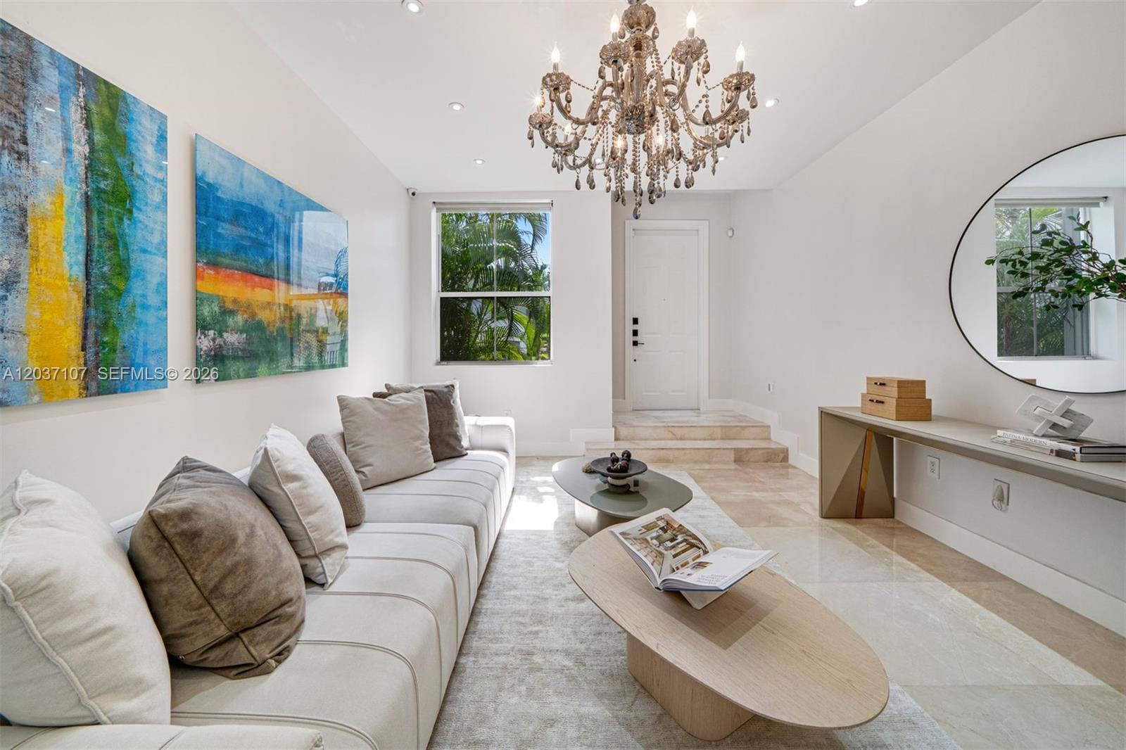 A bright living room features a crystal chandelier, a long beige sofa, and marble flooring — 21156 NE 33rd Ave, Aventura FL 33180, AVENTURA, FL