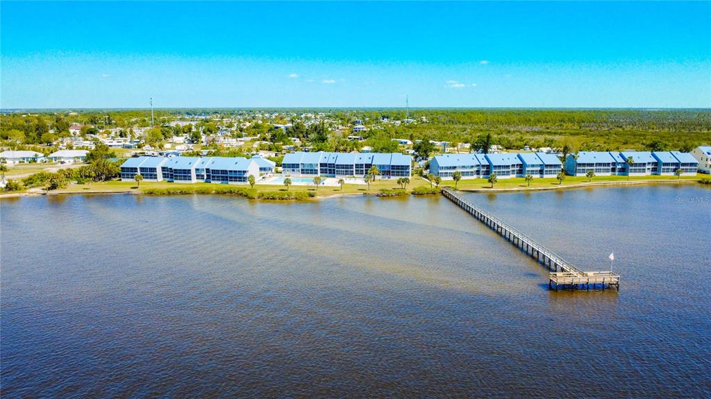 An aerial view shows waterfront apartment buildings with a long pier extending into the water — 4410 WARREN AVENUE UNIT 101, PORT CHARLOTTE, FL