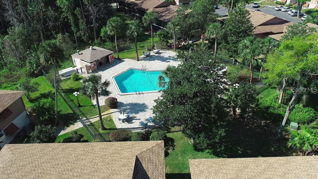 An aerial view of a community swimming pool surrounded by palm trees and apartment buildings — 180 MAGNOLIA WOODS COURT UNIT 9C, DELTONA, FL