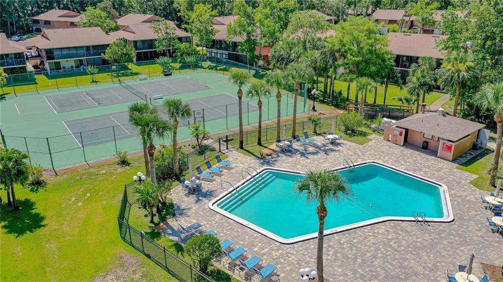 An aerial view shows a swimming pool and tennis courts surrounded by residential buildings and trees — 180 MAGNOLIA WOODS COURT UNIT 9C, DELTONA, FL
