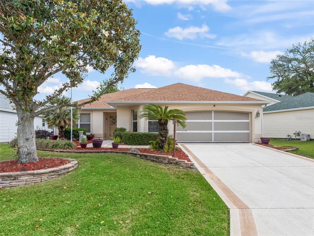 A single-story house with a tan exterior, a two-car garage, and a landscaped front yard — 17325 SE 91ST LEE AVENUE, THE VILLAGES, FL