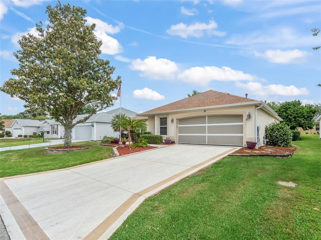 A single-story house with a beige exterior, a two-car garage, and a concrete driveway — 17325 SE 91ST LEE AVENUE, THE VILLAGES, FL