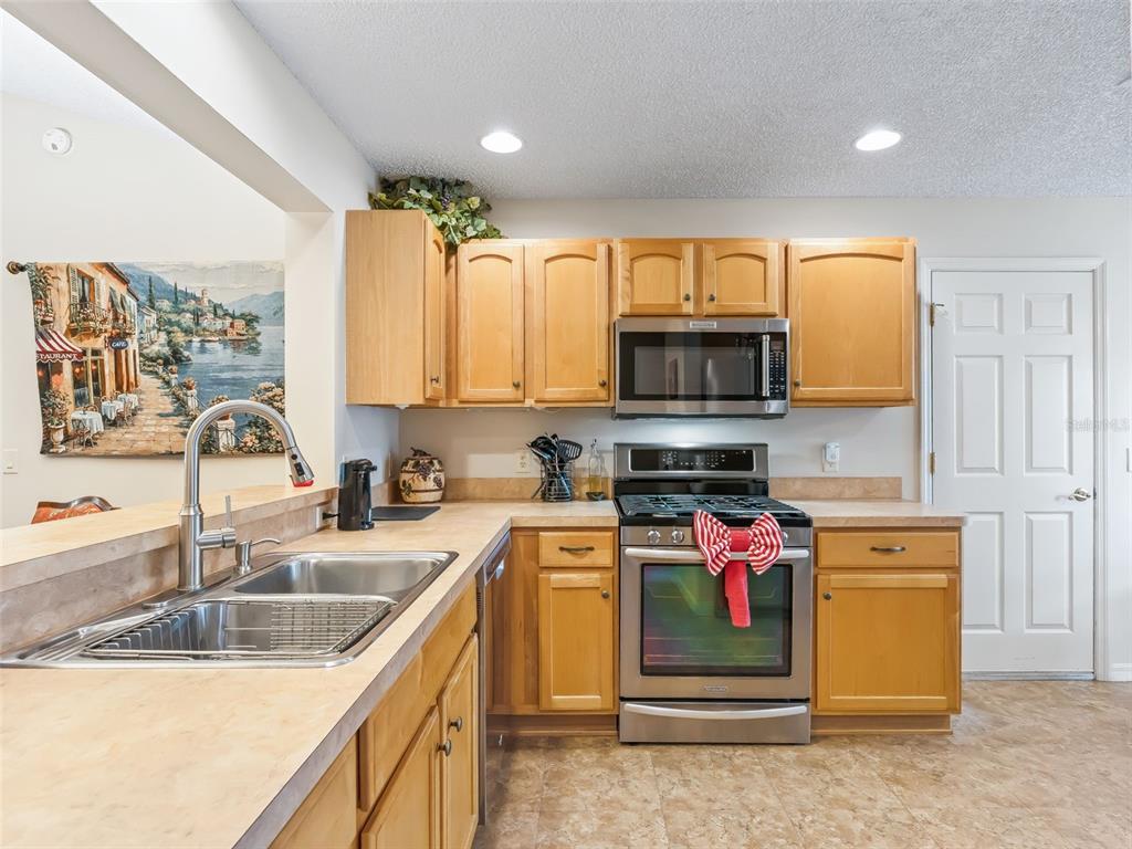 A kitchen features light wood cabinets, stainless steel appliances, and beige laminate countertops — 17325 SE 91ST LEE AVENUE, THE VILLAGES, FL