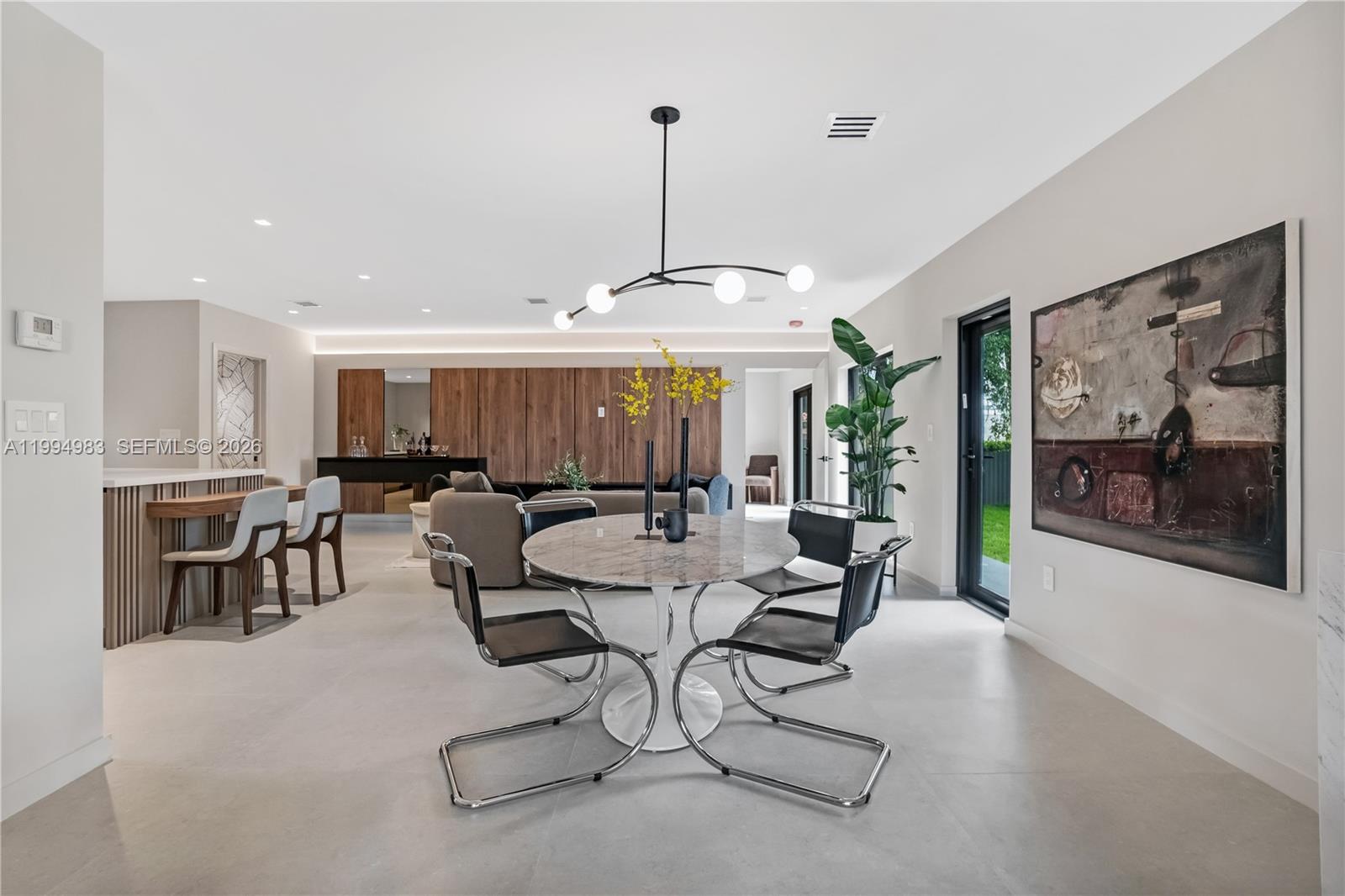 A modern dining area features a marble pedestal table, chrome chairs, and wood wall paneling — 6207 SW 10th St, West Miami FL 33144, WEST MIAMI, FL