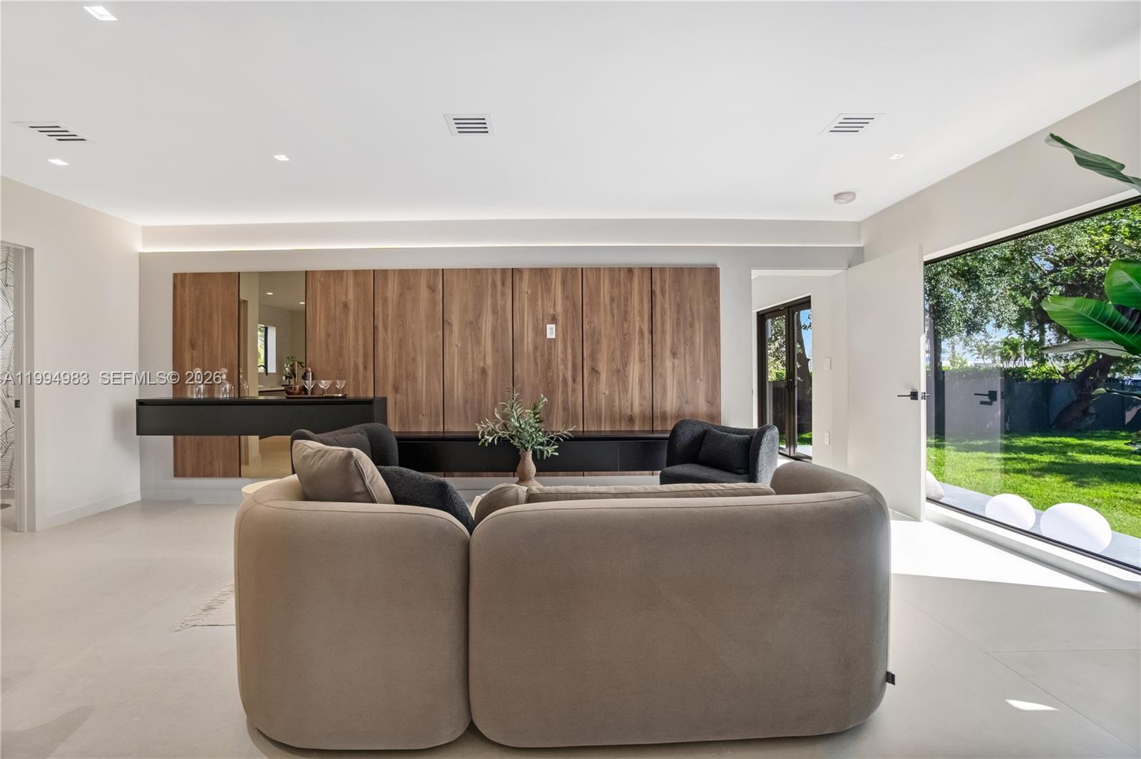 A modern living room features a wood-paneled wall, a floating black console, and large windows — 6207 SW 10th St, West Miami FL 33144, WEST MIAMI, FL