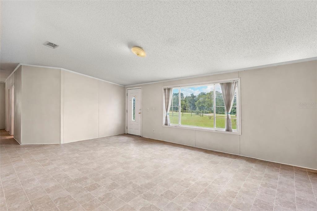 An empty room with light-colored walls, tile flooring, a large window, and a front door — 13317 MOON ROAD, BROOKSVILLE, FL