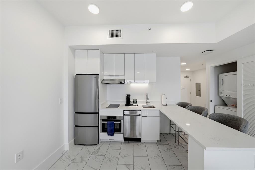 A modern kitchen features white cabinetry, stainless steel appliances, and a white quartz breakfast bar — 411 E SHORE DRIVE UNIT 713, CLEARWATER BEACH, FL
