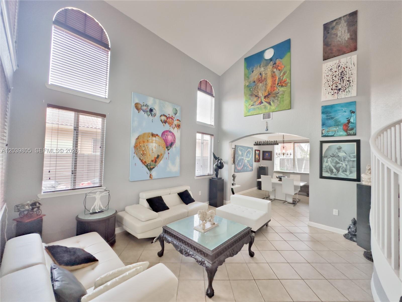 A high-ceilinged living room features white leather sofas, a glass-topped coffee table, and large artwork — 2105 NE 38th Rd, Homestead FL 33033, HOMESTEAD, FL