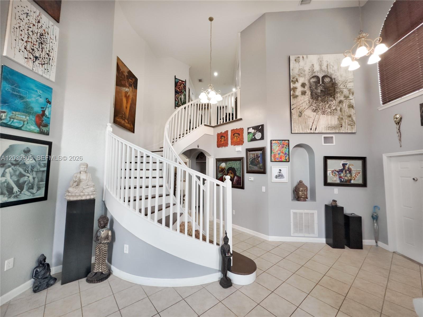 A grand foyer features a curved staircase, tiled floors, and numerous pieces of wall art — 2105 NE 38th Rd, Homestead FL 33033, HOMESTEAD, FL