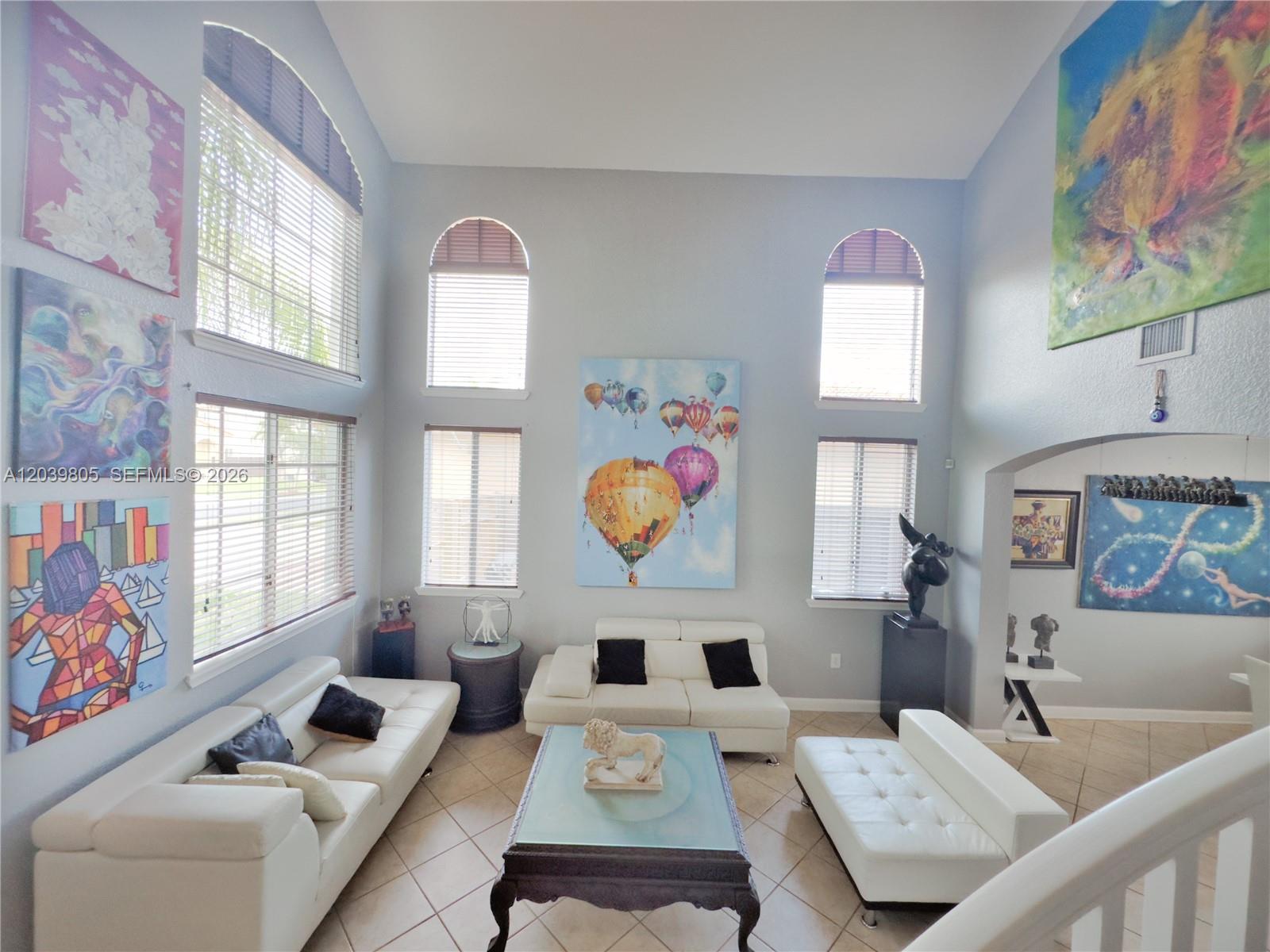 A high-ceilinged living room features white leather sofas, a glass-topped coffee table, and colorful artwork — 2105 NE 38th Rd, Homestead FL 33033, HOMESTEAD, FL