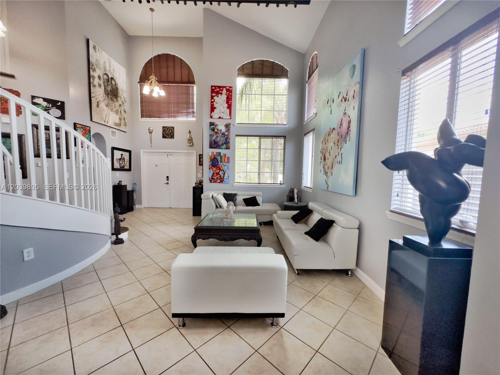 A high-ceilinged living room features white leather furniture, tile flooring, and large wall art — 2105 NE 38th Rd, Homestead FL 33033, HOMESTEAD, FL