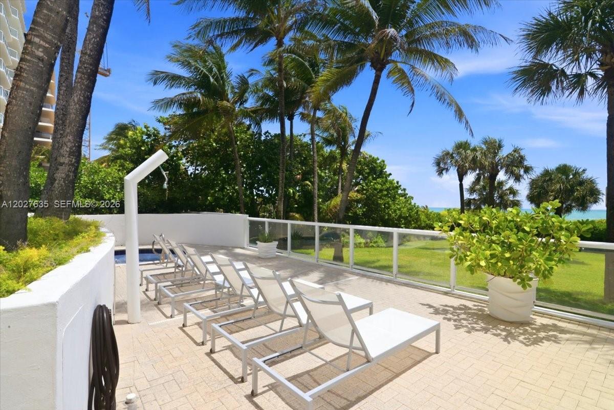 A paved patio features lounge chairs, a shower, and a glass railing overlooking the ocean — 8911 Collins Ave # 601, Surfside FL 33154, SURFSIDE, FL
