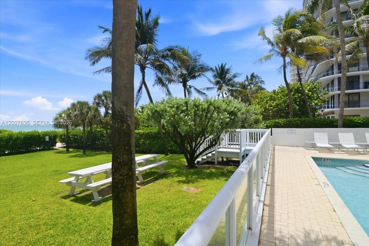 A grassy lawn with picnic tables sits beside a swimming pool near the ocean — 8911 Collins Ave # 601, Surfside FL 33154, SURFSIDE, FL