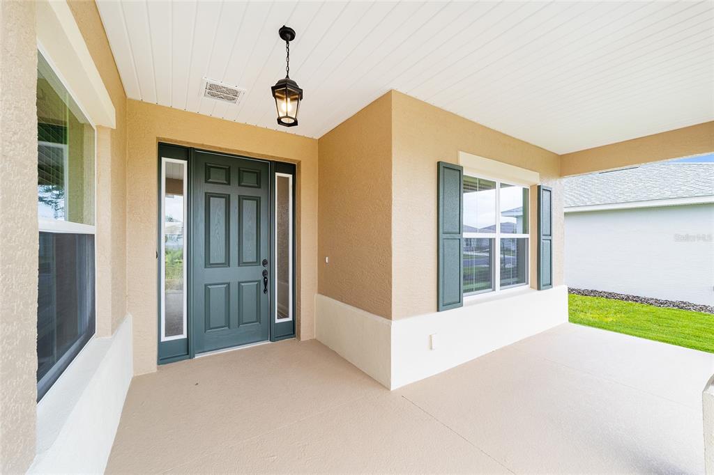 A covered front porch features a dark green front door with sidelights and a lantern light — 10001 SW 106TH CIRCLE, OCALA, FL
