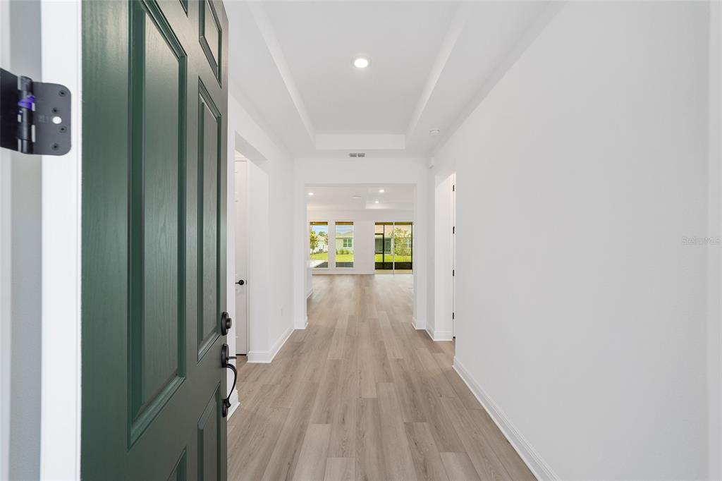 A view from an open green front door into a bright hallway with wood floors — 10001 SW 106TH CIRCLE, OCALA, FL