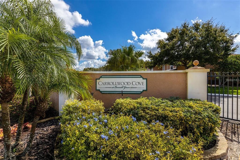 A sign for Carrollwood Cove at Emerald Green stands before a gated entrance and landscaping — 14810 PAR CLUB CIRCLE, TAMPA, FL