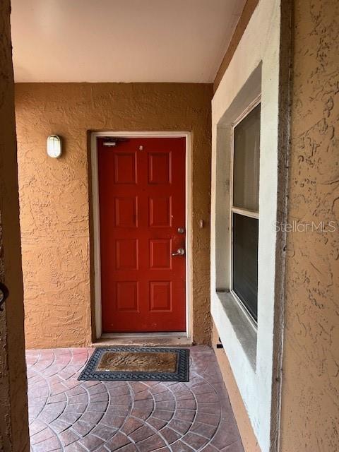 A red front door is centered on a textured tan wall with a patterned patio — 14810 PAR CLUB CIRCLE, TAMPA, FL