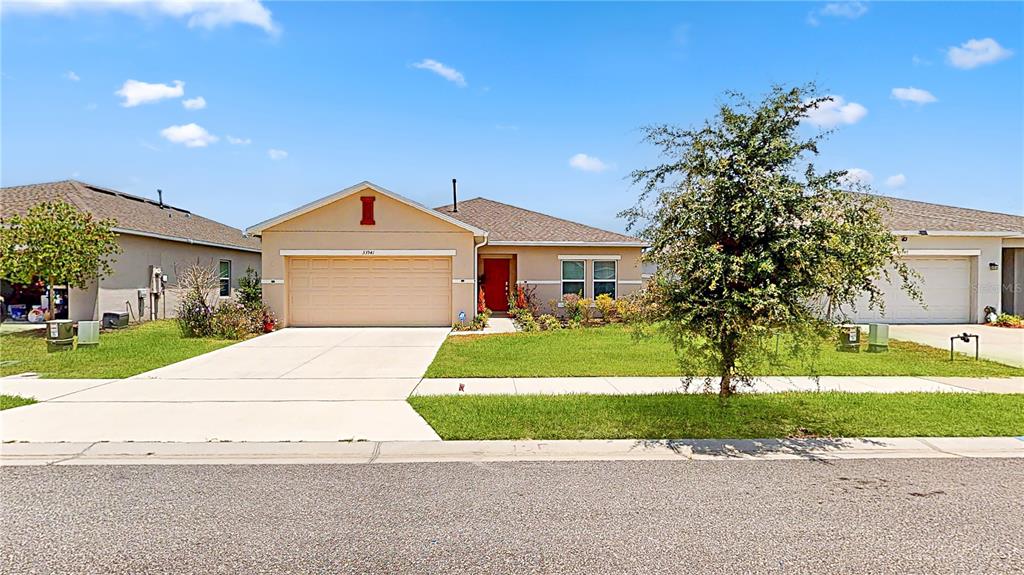 A single-story house with a beige exterior, a red front door, and a concrete driveway — 33941 SKY BLOSSOM CIRCLE, LEESBURG, FL