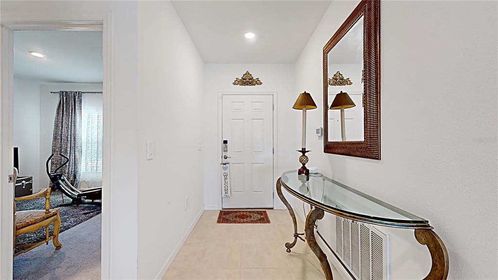 A bright entryway features a glass-topped console table, a wall mirror, and a white door — 33941 SKY BLOSSOM CIRCLE, LEESBURG, FL