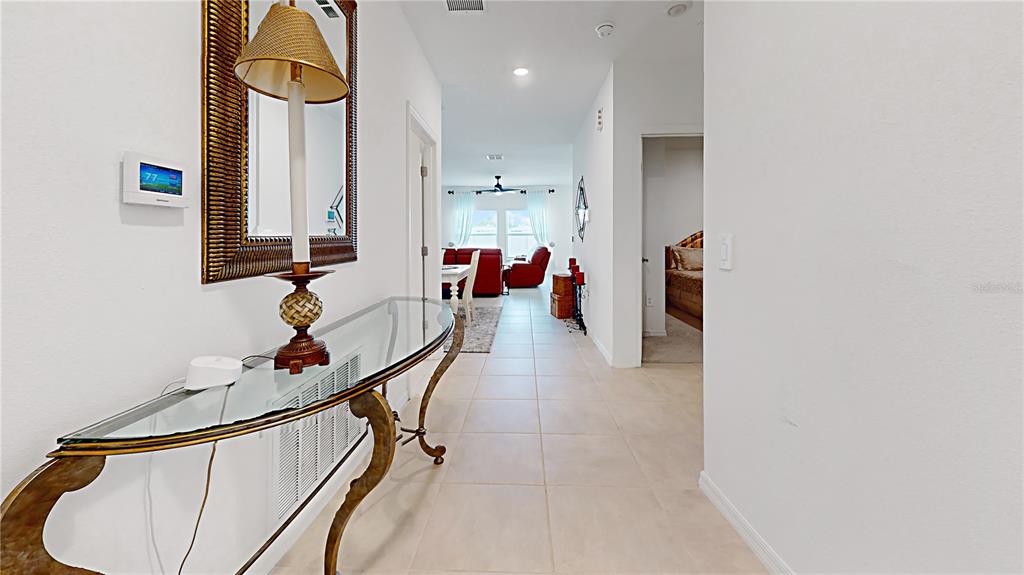 A hallway with a glass console table leads to a living area with tile flooring — 33941 SKY BLOSSOM CIRCLE, LEESBURG, FL
