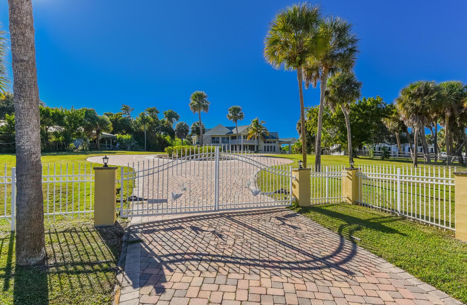 A white metal gate opens to a paved driveway leading toward a large house — 3343 S Indian River Drive, Fort Pierce FL 34982, FORT PIERCE, FL