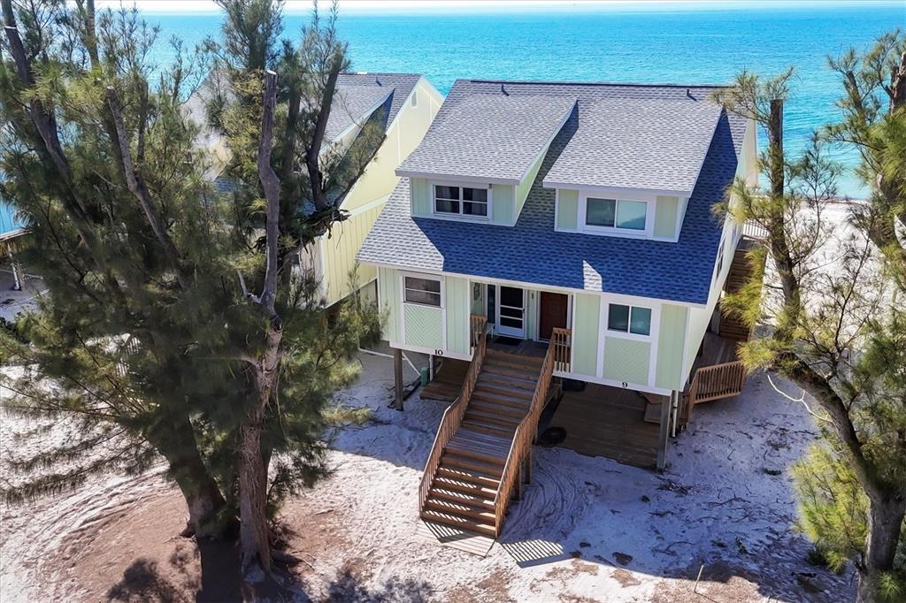 An elevated, light green beach house with a shingled roof stands on sandy ground — 301 S GULF BOULEVARD UNIT 10, PLACIDA, FL
