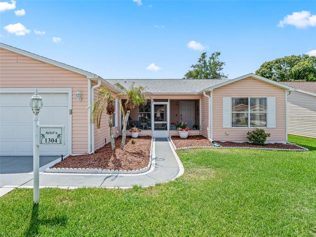 A single-story house with light pink siding, a white garage door, and a front porch — 1304 GUADALUPE COURT, THE VILLAGES, FL
