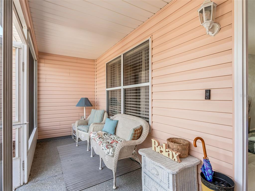 A covered porch features light-colored siding, wicker furniture, a striped rug, and a screen door — 1304 GUADALUPE COURT, THE VILLAGES, FL
