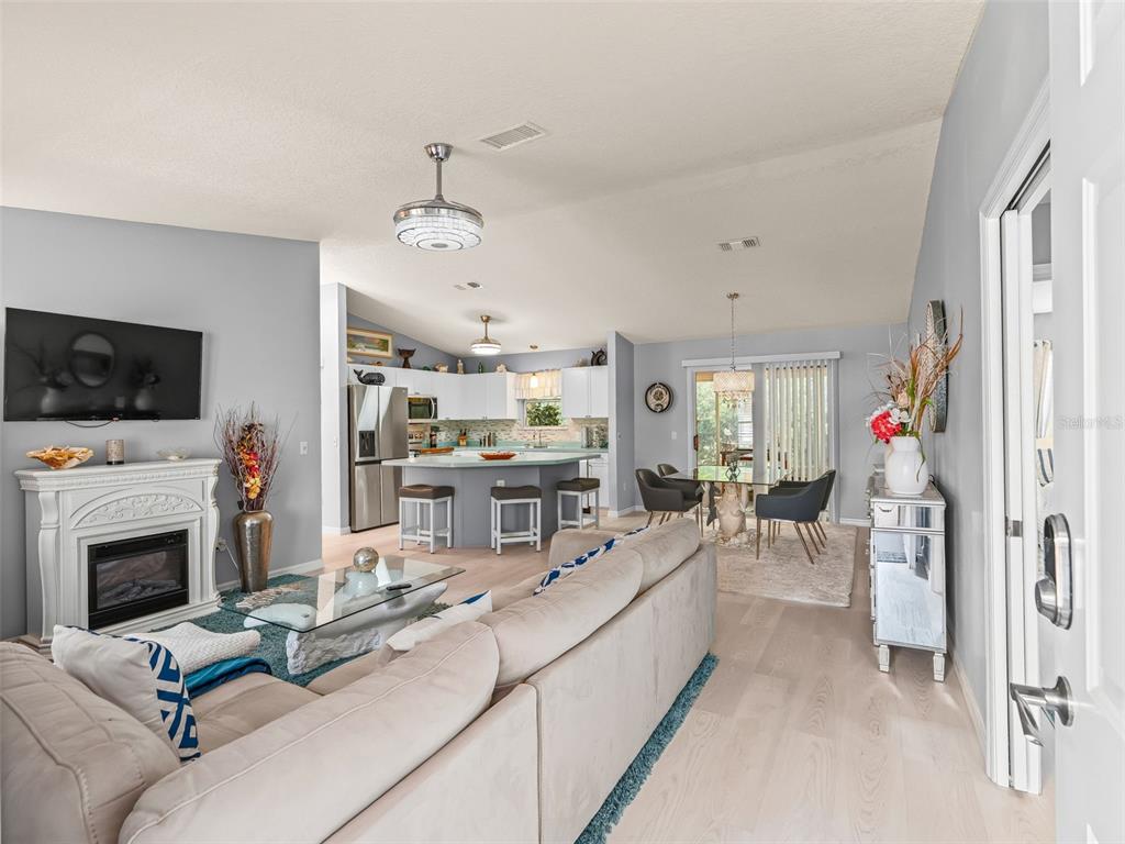 An open-concept living room and kitchen featuring light wood floors and a white fireplace — 1304 GUADALUPE COURT, THE VILLAGES, FL
