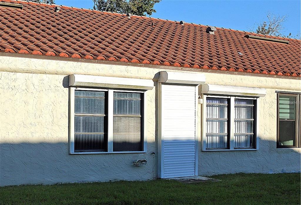 A patio area features a blue awning, string lights, decorative signs, and three colorful croton bushes — 8804 40TH LANE N, PINELLAS PARK, FL