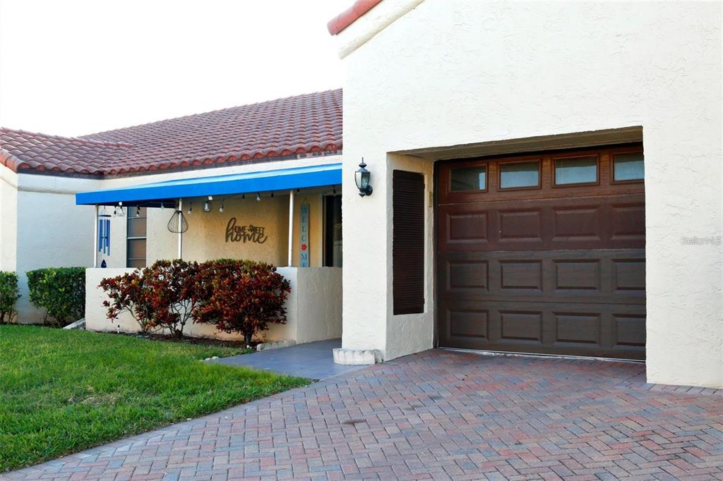 A single-story house with a brick driveway, blue awning, and exterior lighting at dusk — 8804 40TH LANE N, PINELLAS PARK, FL